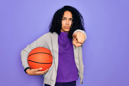 做运动的非洲裔美国卷发女运动员在紫色背景上拿着篮球图片