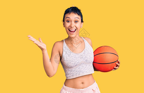 拿着篮球的年轻女子用快乐的微笑和胜利者的表情用举起的图片