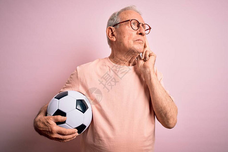 头发灰白的高级足球运动员在粉红色的孤立背景上拿着足球图片