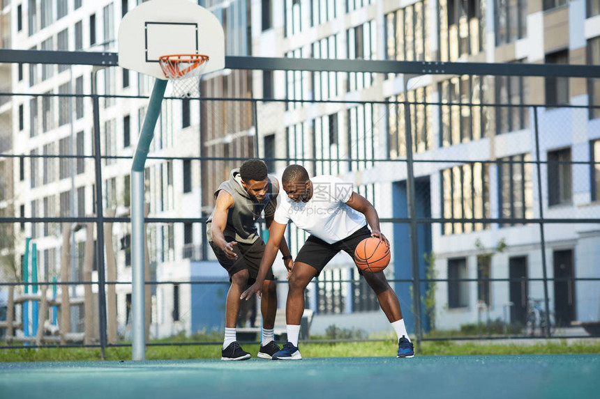 两名非裔美国人在城市环境复制空间的户外法庭上打篮球的宽角图片