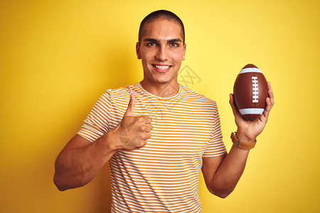 年轻的橄榄球运动员在黄色的孤立背景上拿着足球图片