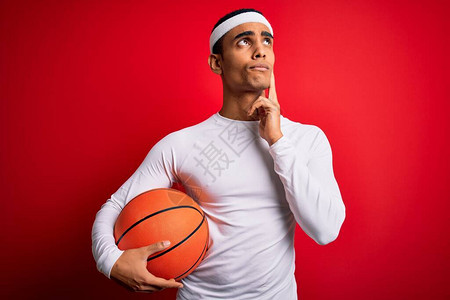 年轻英俊的非洲裔美国运动员拿着篮球在红色背景下严肃地思考问题图片