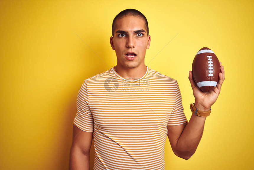年轻的橄榄球运动员在黄色孤立的背景上拿着一个足球图片