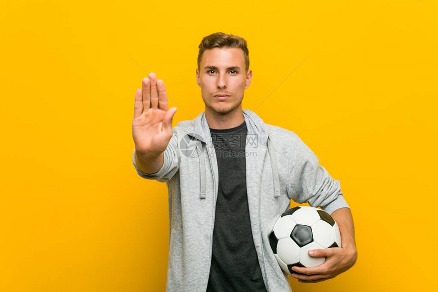 年轻caucasian男子拿着足球站在伸展的手举起手来图片