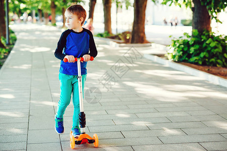 可爱的男孩骑在夏日公园的滑板车上健康的生活方式和运动休闲孩子在户外度过活跃的时间孩子们学习滑旱冰背景图片