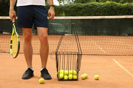 男子用一篮网球在红土场上拿着球拍图片