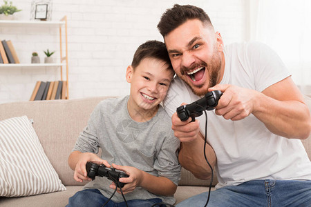 呆在家里玩得开心爸和儿子用操纵杆在家玩电子游图片