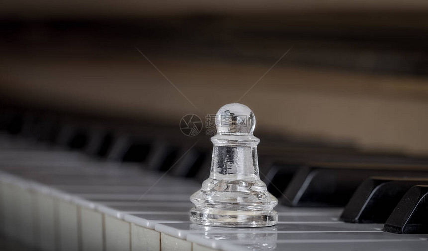 透明的玻璃棋子Pawn站在一架旧木钢琴的键上特写镜头图片
