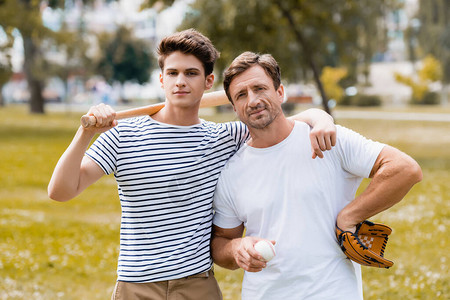带着垒球棒的少年男孩站在父亲身边身着皮图片