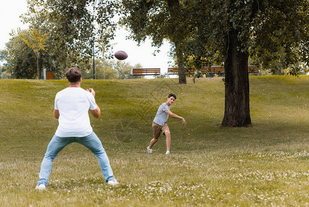 在绿公园和父亲一起玩美式足球的少年男孩有图片