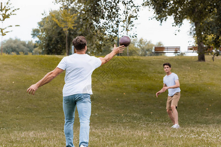 父亲在绿公园向少年儿子扔橄榄球时有图片