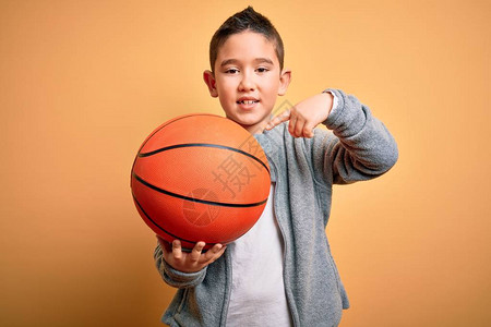小男孩在孤立的黄色背景上玩篮球比赛图片