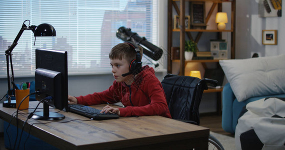 一名年轻残疾男孩坐在轮椅上玩电子游戏的图片