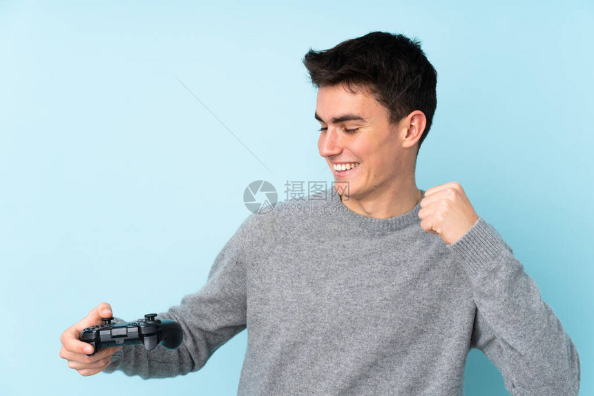 与一个视频游戏控制器玩耍的青少年caucasian男子在庆祝胜利的蓝图片