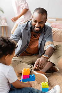 坐在靠近儿子的地板上玩砖块游戏的年轻非洲裔美国父亲的图片