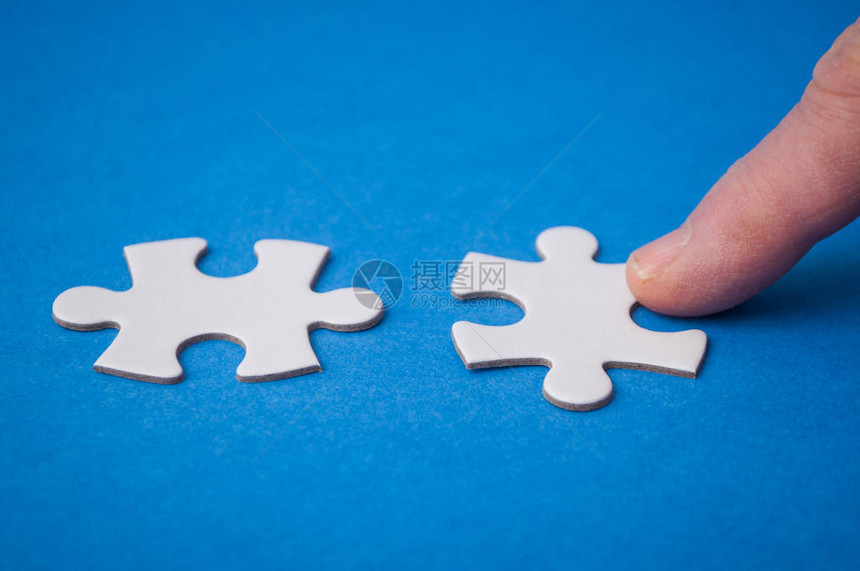 在蓝色背景上用手连接两个拼图块的人特写镜头在团队合作中找到正确解图片
