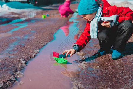 儿童在春季水坑中玩纸船儿图片