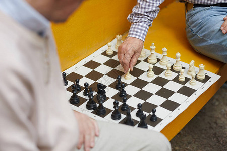 在黄色长凳上下棋时老象棋玩家的图片