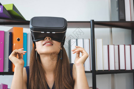 轻松的亚洲年轻女在办公室工作场合戴虚拟VR现实眼镜背景图片