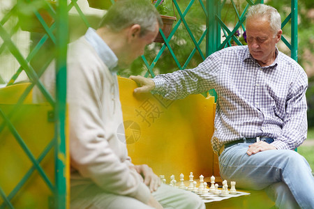 两个老朋友在外面下象棋坐在绿色开阔公园的黄色长椅上图片
