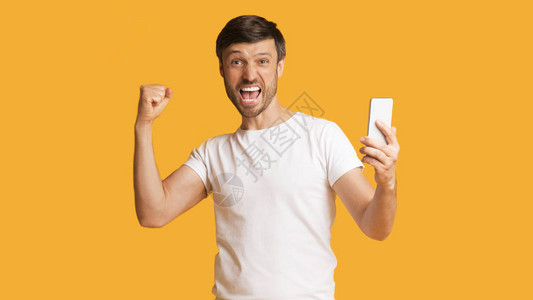 欢庆成功情绪家伙尖叫手机掌声在工作室的黄色背景上摇图片