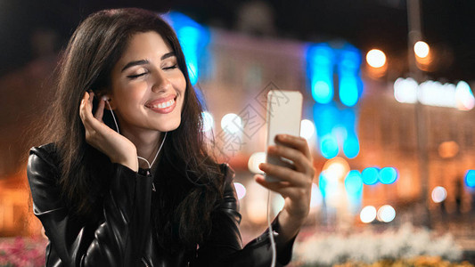 梦中女孩在手机上享受歌声晚上在城图片