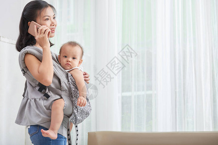 年轻亚洲妇女带着婴儿在摇和打电图片