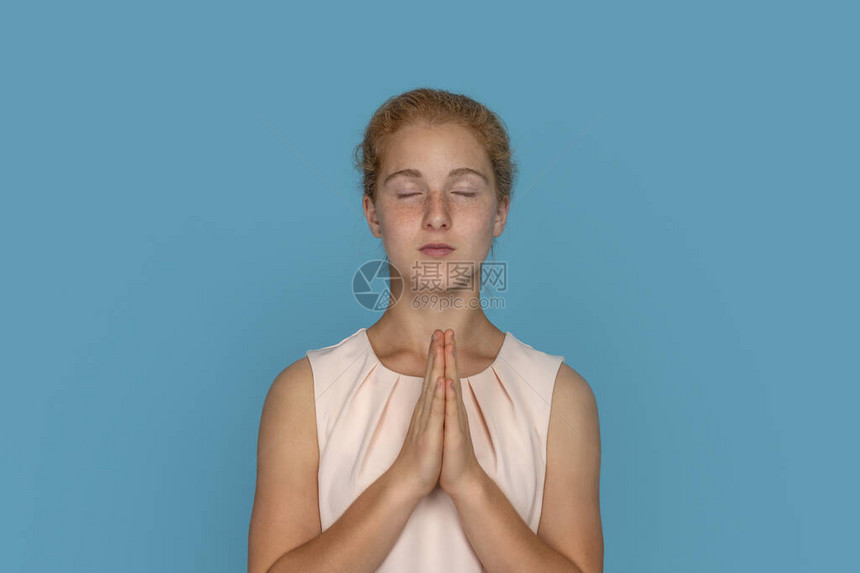 红头发女孩在摄影棚的蓝色背景下闭着眼睛祷告图片