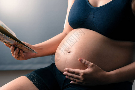 读一本书的孕妇专注于她的腹部图片