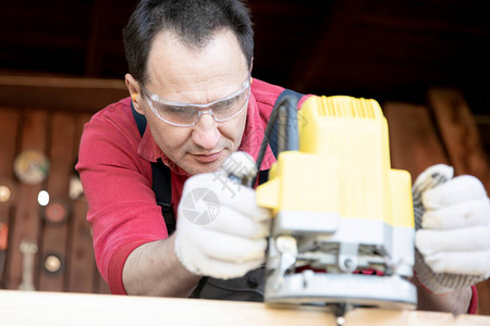 英俊的中年木匠用铣削工具在木制工件上工作用铣削木工机加工天然木梁图片
