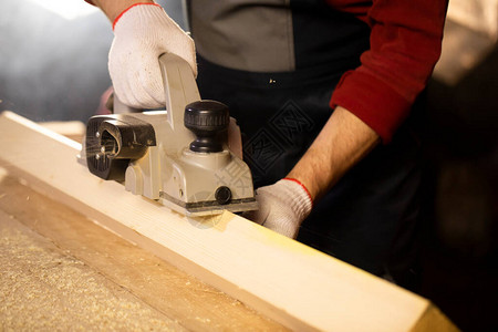 特写电动刨子倒角木制工件木工在小屋车间工作台上的木头上工作在图片