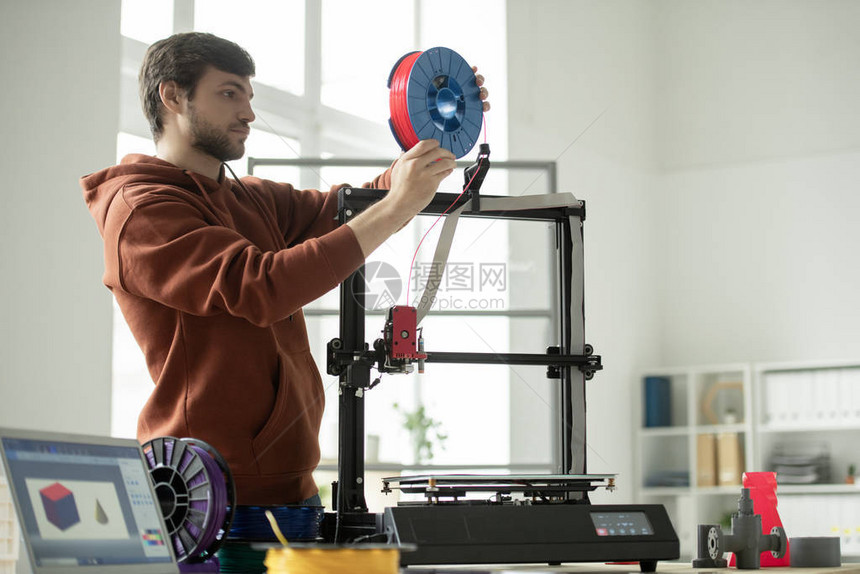 年轻人在打印几何数字的同时在3D打印机中用红色丝图片