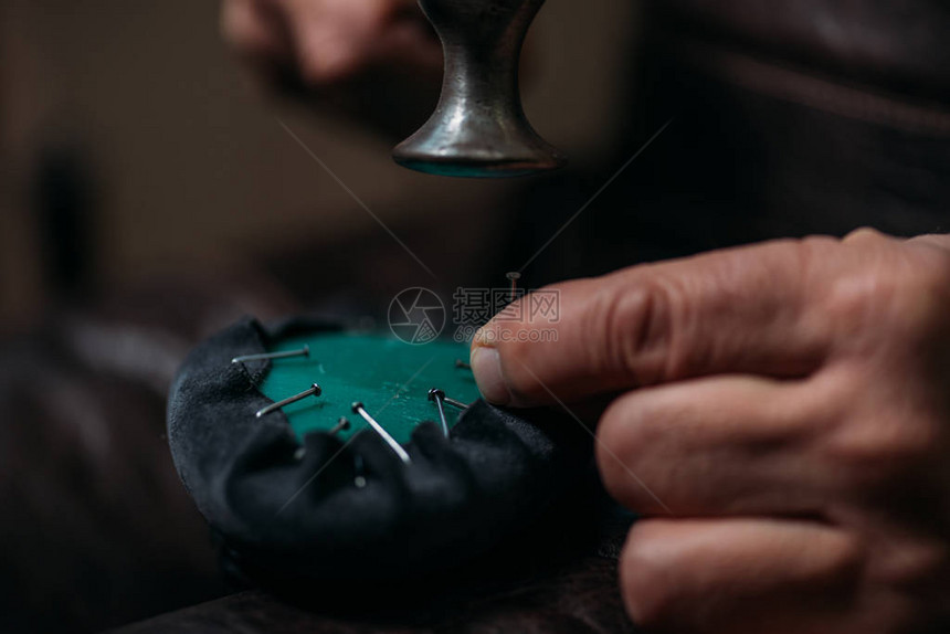 鞋匠在车间用钉子将皮革固定在鞋上的剪影图片