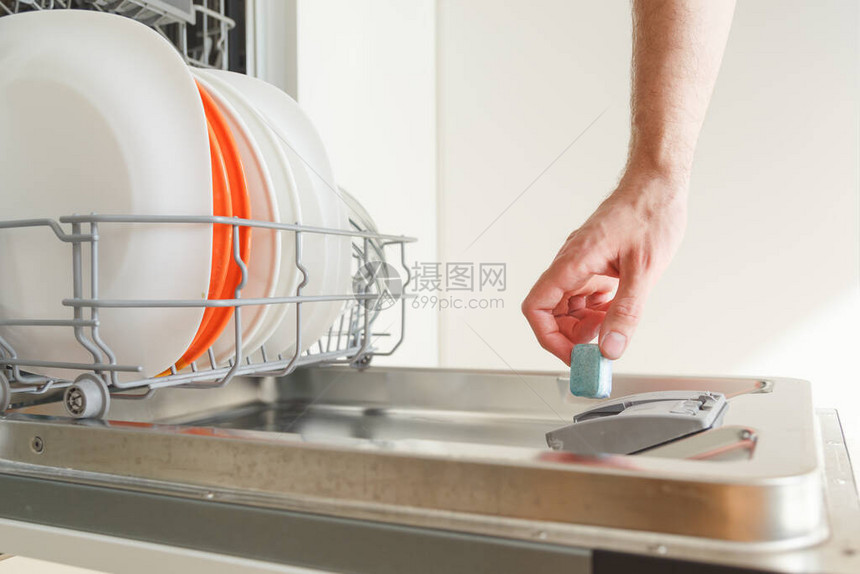男人把一个化学洗碗机平板电脑放进洗碗机里图片