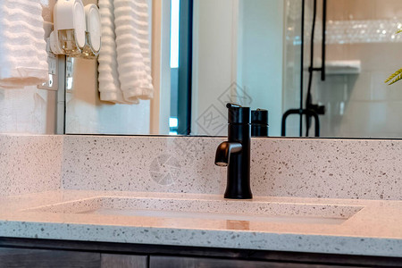 带有黑色水龙头的台下水槽位于家庭浴室内的白色台面上墙上的镜子映出挂着的毛巾敞开的门背景图片