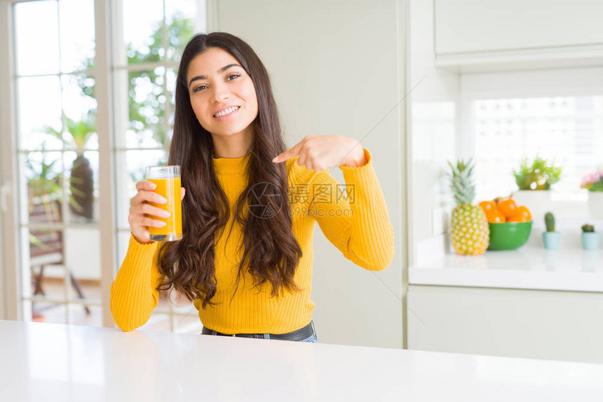 年轻女子喝了一杯新鲜橙汁脸上有惊喜的笑脸指着图片