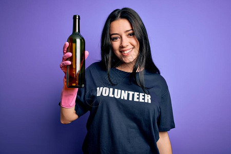 身穿志愿者T恤的褐发年轻女子在紫色背景中采摘玻璃瓶图片