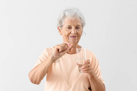 浅色背景中带药丸和一杯水的老妇人图片