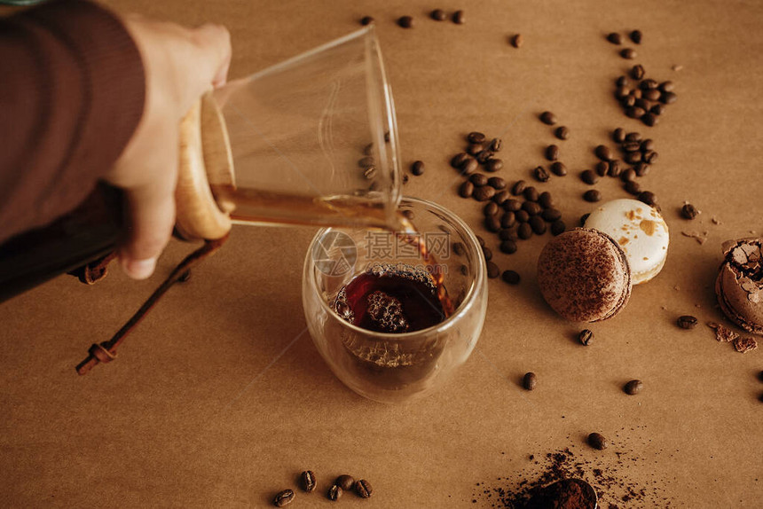 制作滴漏咖啡用咖啡烤豆马卡龙巧克力从棕色背景的杯子里的玻璃瓶中手工倒出新鲜咖啡时尚的形象图片