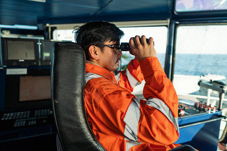 穿着工作服的船或桥上的菲律宾甲板官员他正在通过双筒望远镜看COLREG背景图片