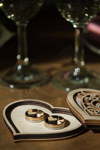 金婚戒指在一个木盒子里雕刻在心脏的形状上香槟杯放在背景上图片