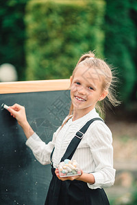 快乐的小女学生有粉笔和黑板背景回到图片
