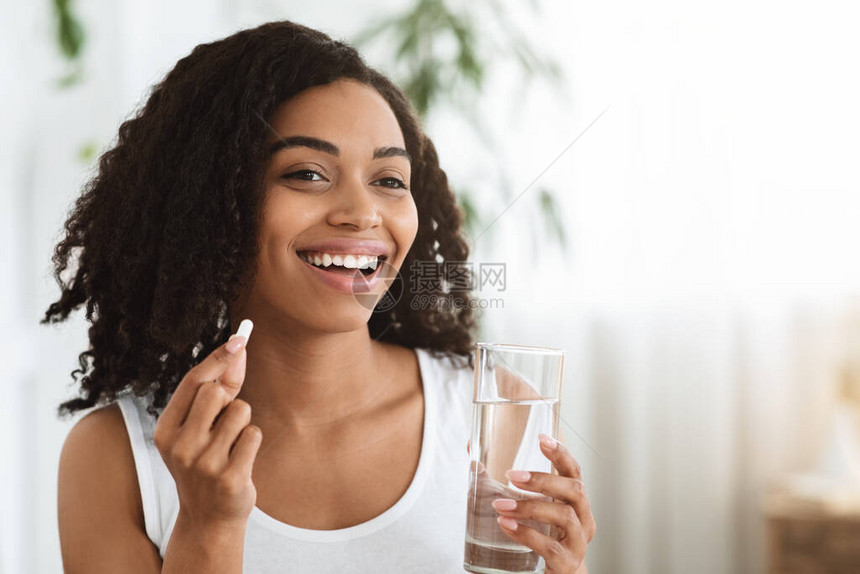 健康饮食营养微笑的非洲女人的肖像拿着维生素丸和一杯矿泉图片