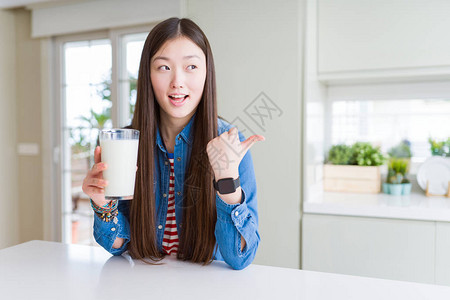 美丽的亚洲女喝着一杯新鲜的牛奶指尖和展示用大拇指举到旁边面图片