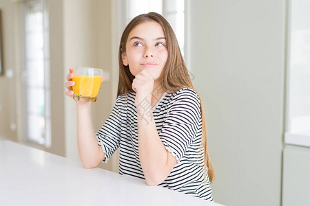 美丽的年轻女孩喝着一杯新鲜橙子汁严肃的面孔思考问题非常困惑图片