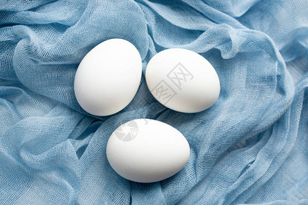 蓝色精致纺织纱布上的三个白色生鸡蛋或煮鸡蛋图片