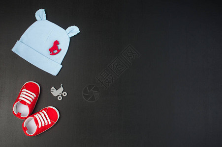 黑色粉笔板背景的红婴儿靴子帽子和婴儿附件图片