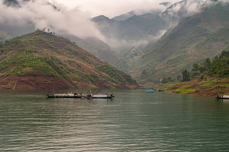 大宁河上的滴翠峡谷广阔的风景与工人在小船沿着鱼栏在翡翠绿的水与绿色覆盖的山脉在clouds图片