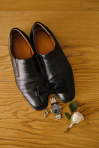 黑色男鞋和领结在木质纹理与袖扣手表和白玫瑰新郎胸花图片