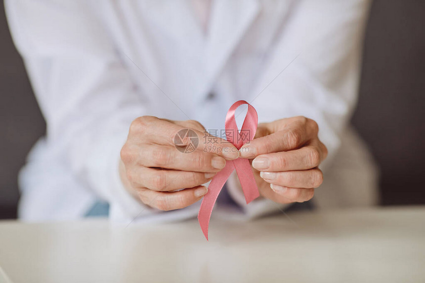 无法辨认的持有粉色丝带与白色实验室大衣对比白外衣作为提高对乳腺癌认识象征的女医生背景近距离图图片